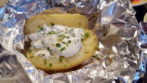 tin foil with an open jacket potato in it with sour cream and chives on it