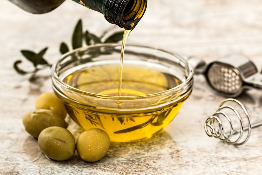 a glass bowl with olive oil in it and a bottle pouring into it with fresh olives next to the bowl