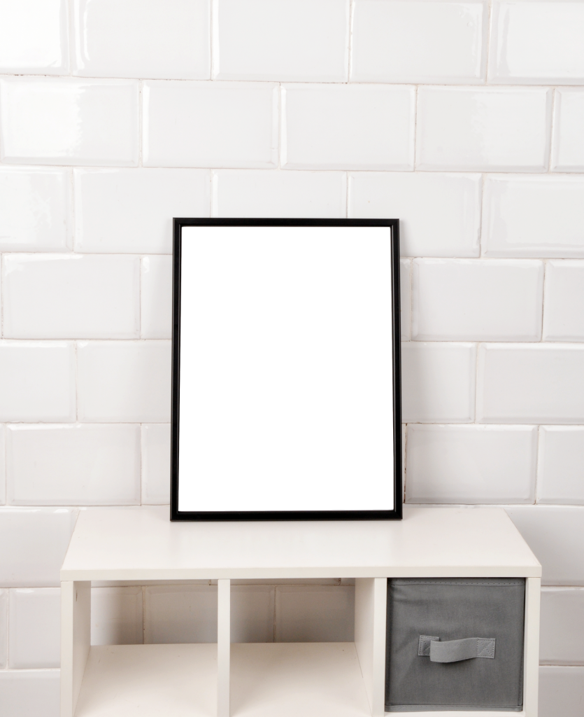 a white brick wall with a white set of shelves in front of it and on top a black picture frame with a plain white picture inside