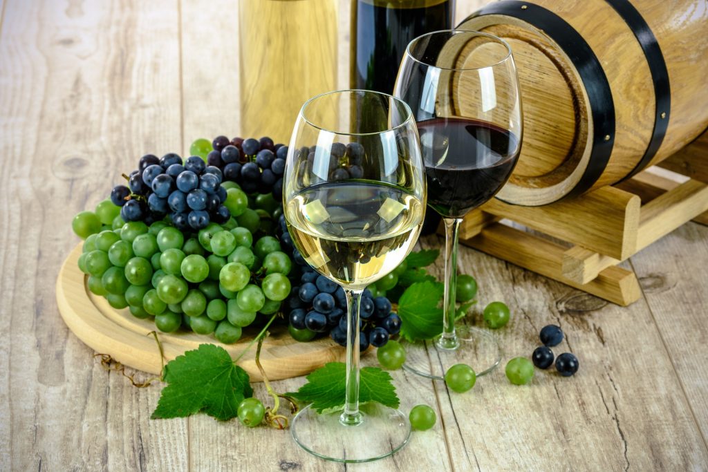 a wooden barrel with green and red grapes in front and 2 glasses one with white and one with red wine