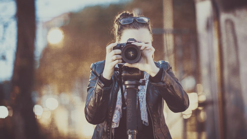a woman in a leather jacket facing the camera holding a camera to her face. a photographer