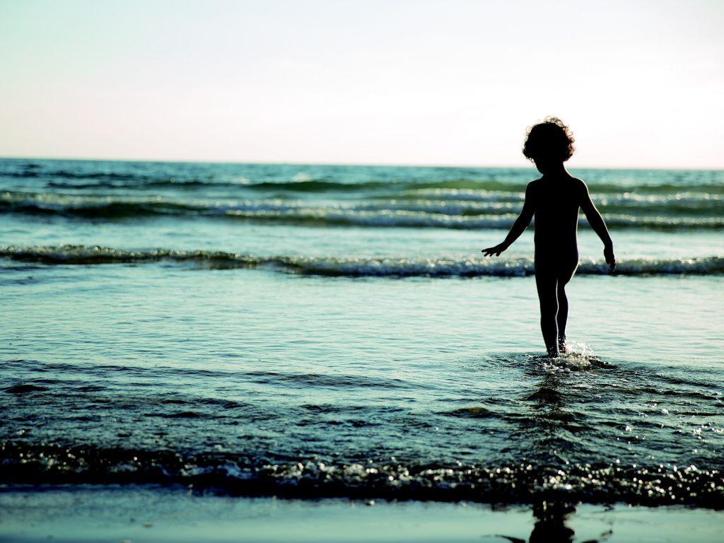 a silhouette picture of a child playing in the small waves of the sea