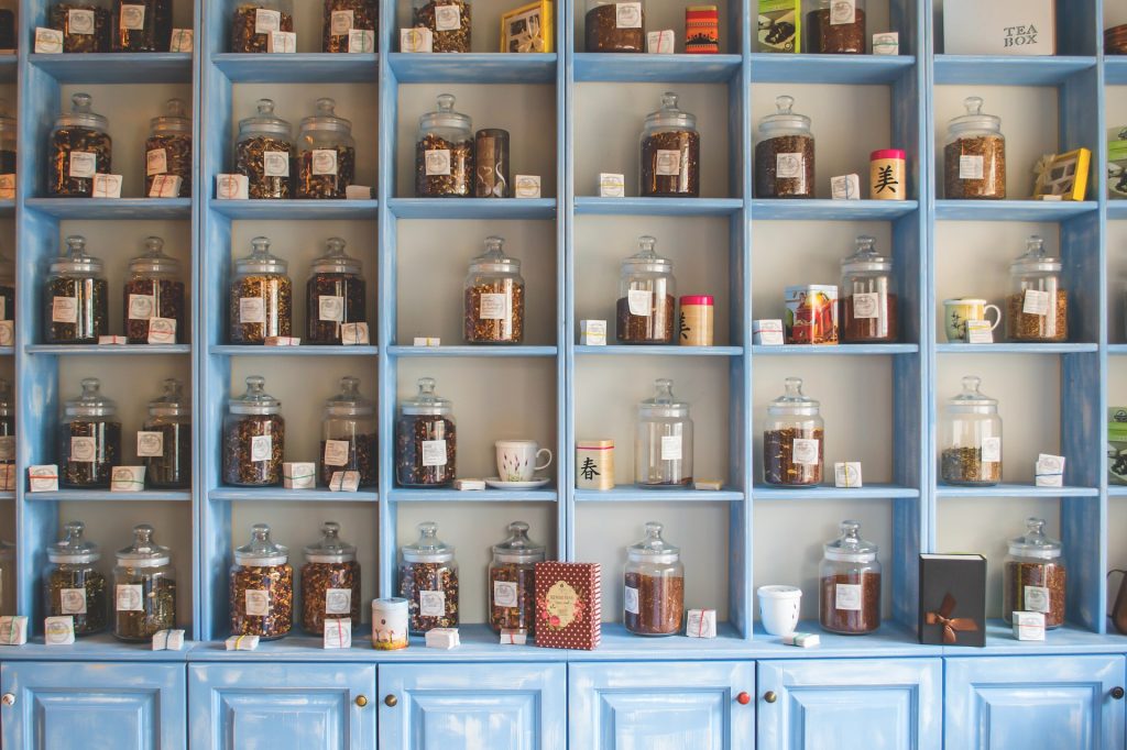 4 stacks of tall blue shelves to the ceiling with cupboards underneath and mason jars with cooking ingredients stood on each shelf