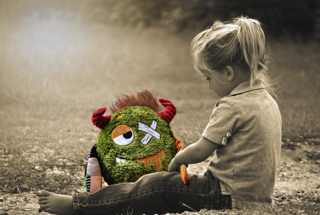 a black and white photo of a little blonde girl sat on a path with a coloured toy that is sad with lots of bandages on