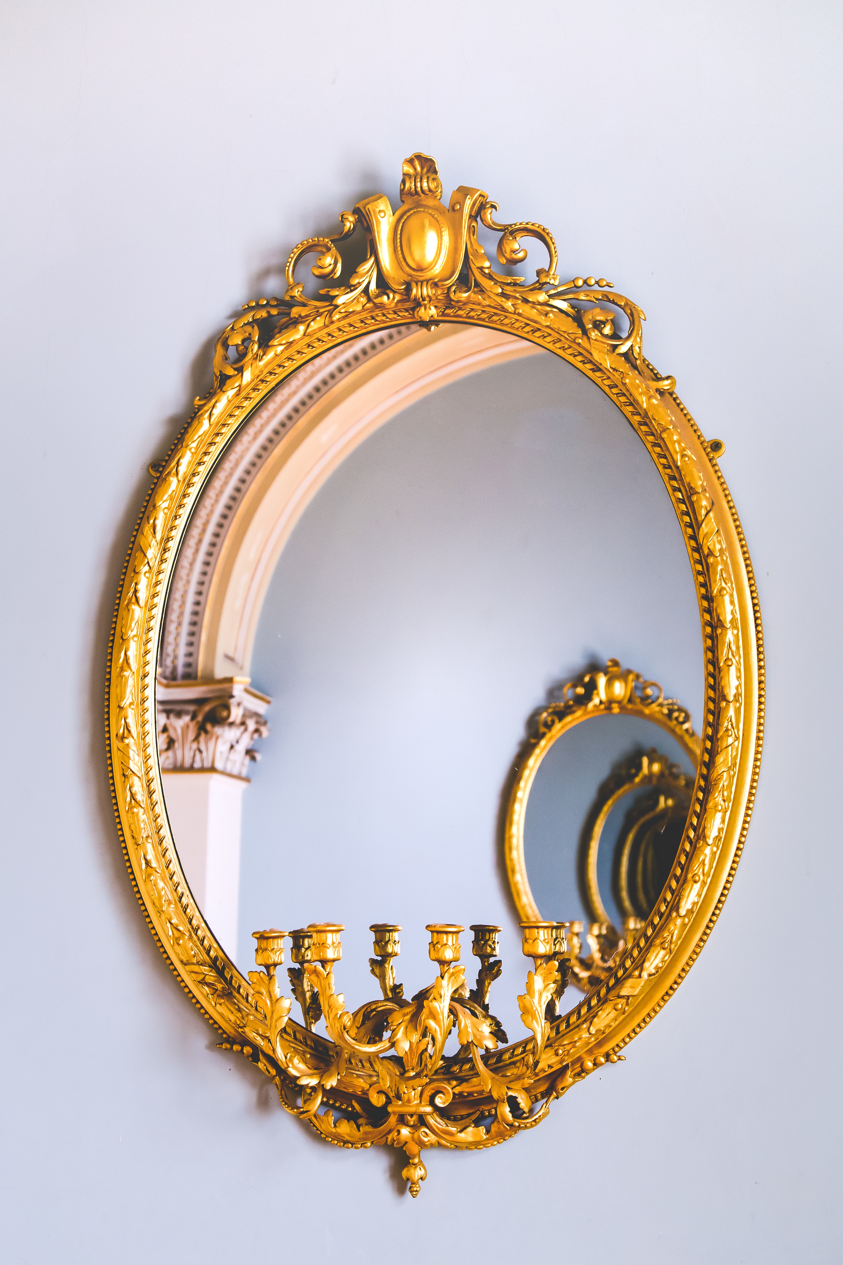 a gold oval mirror on a white wall and in the reflection are several more of the same mirror