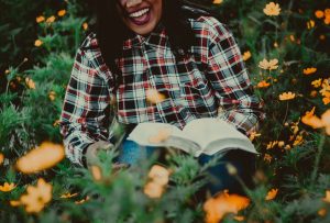 a woman in a plaid shirt sat on grass with a book and laughing