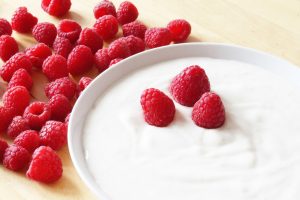 a white bowl full of natural yogurt and toppedwith raspberries
