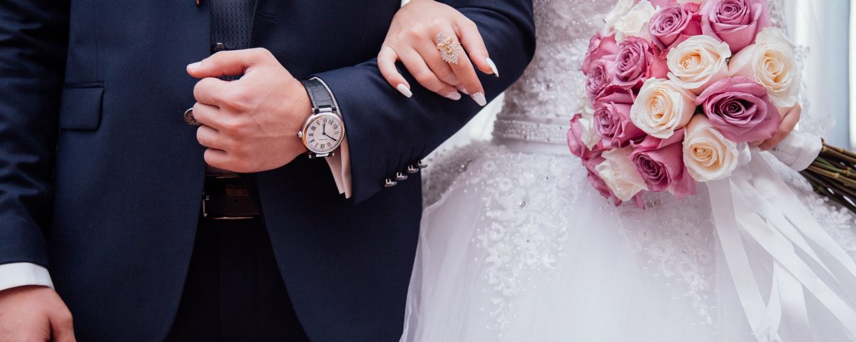 a bride and grooms bodies linked arms in their outfits. bridge is holding pink and white roses