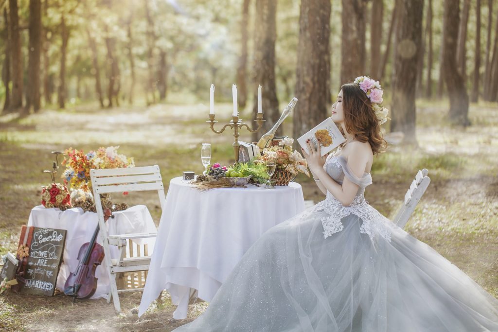 a bride sat a table with champagne and cheese in a garden