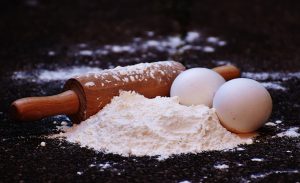 a black surface with a pile of flour, two eggs and a rolling pin