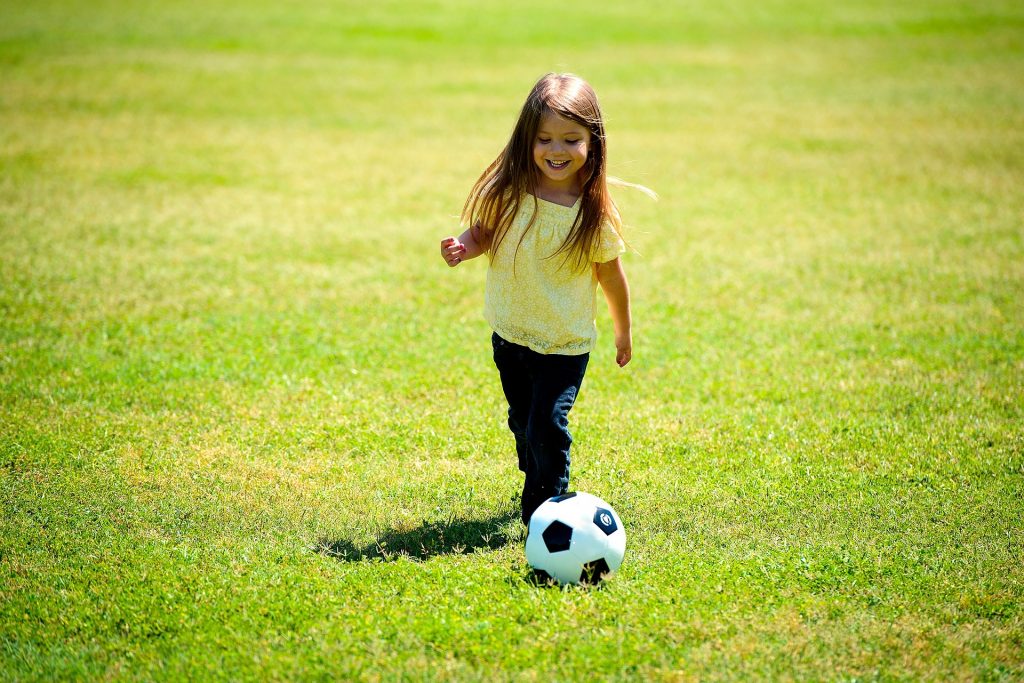 a little girl playing football on the grass