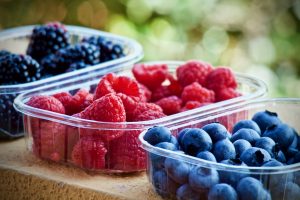 three punnets of fresh fruit on a bench - raspberries, blueberries and blackberries