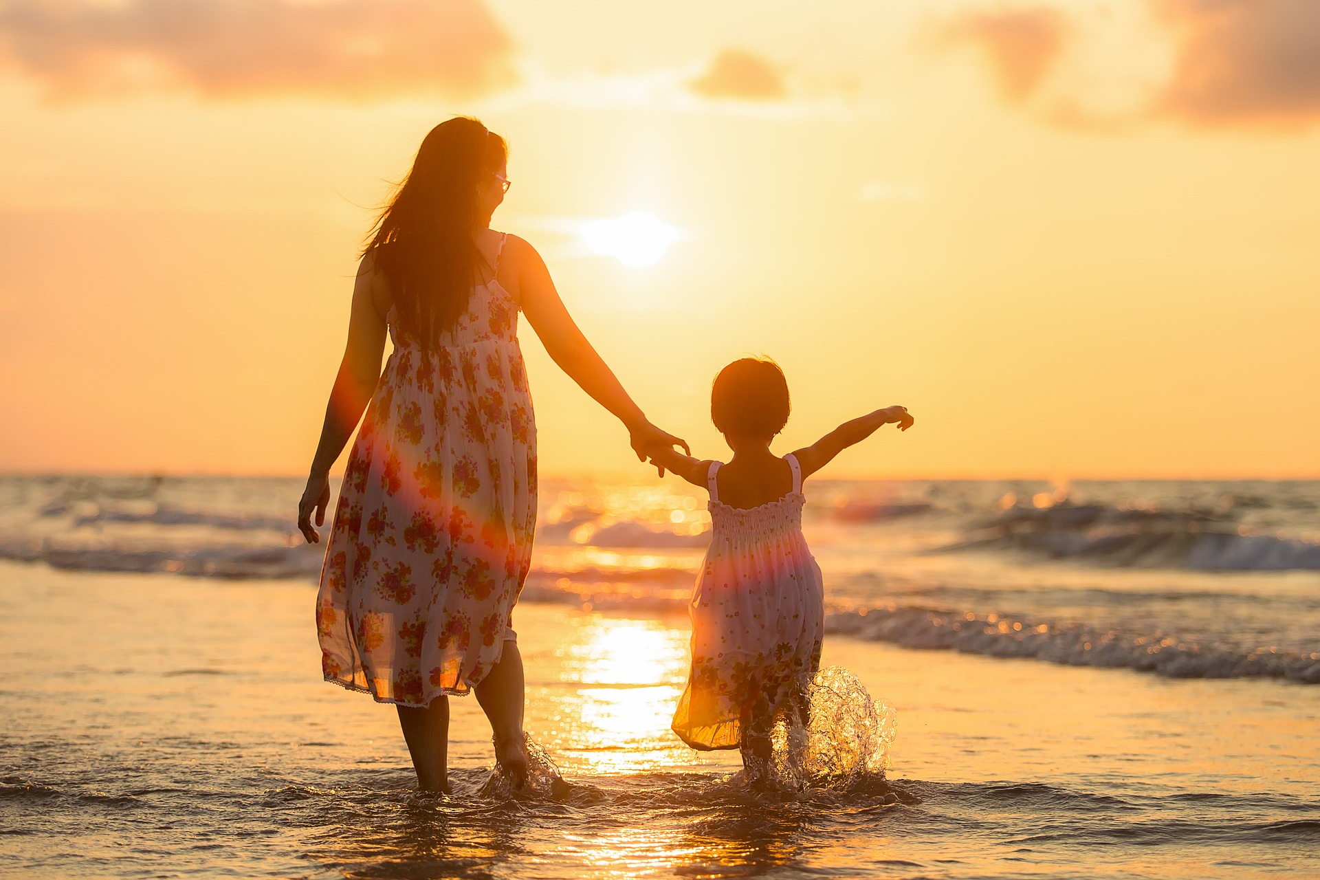 a mother and daughter holding hands walking along the beach at sunset