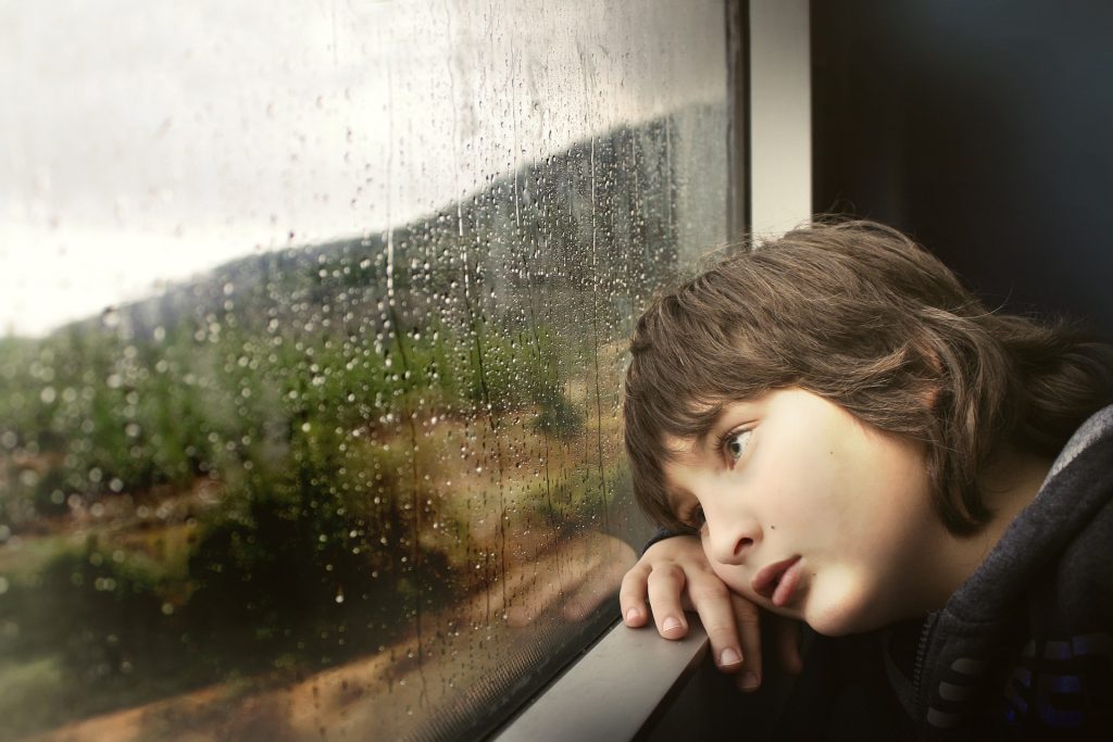 a young boy, bored, staring out of a rain covered window
