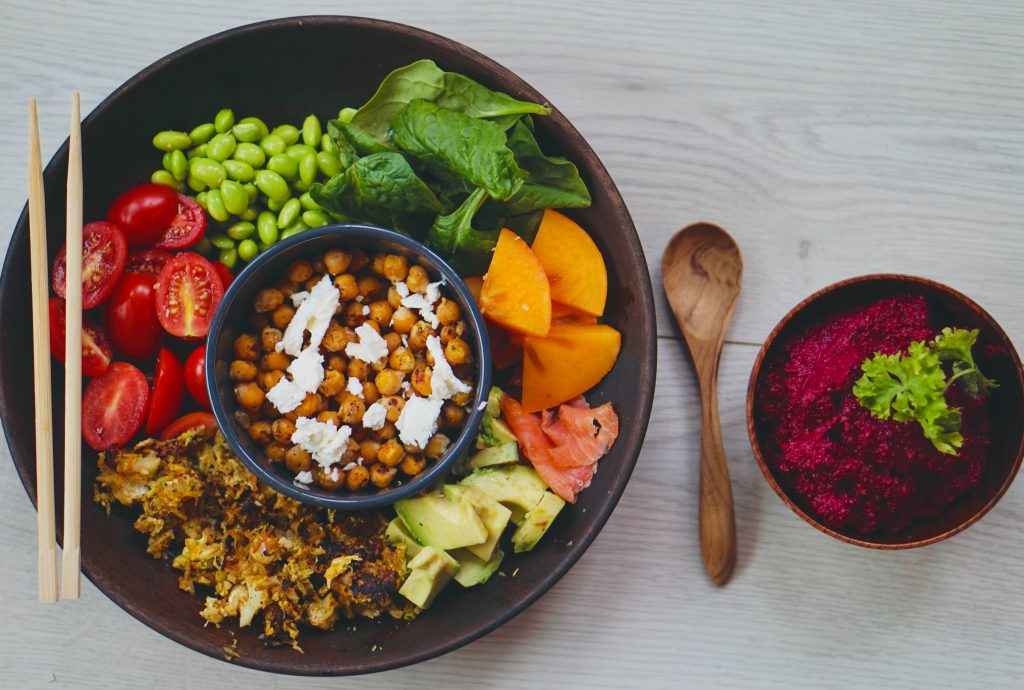 an above shot of a buddha bowl salad with a spoon and beetroot humus next to it