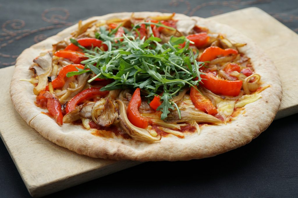 a whole pizza with onions peppers and rocket on a wooden chopping board. vegan