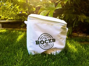 a white cool bag with rocks drinks written on it say on the grass in sunlight