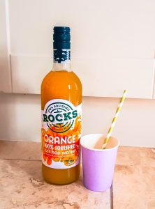 orange rocks drinks next to a cup and straw on marble floor