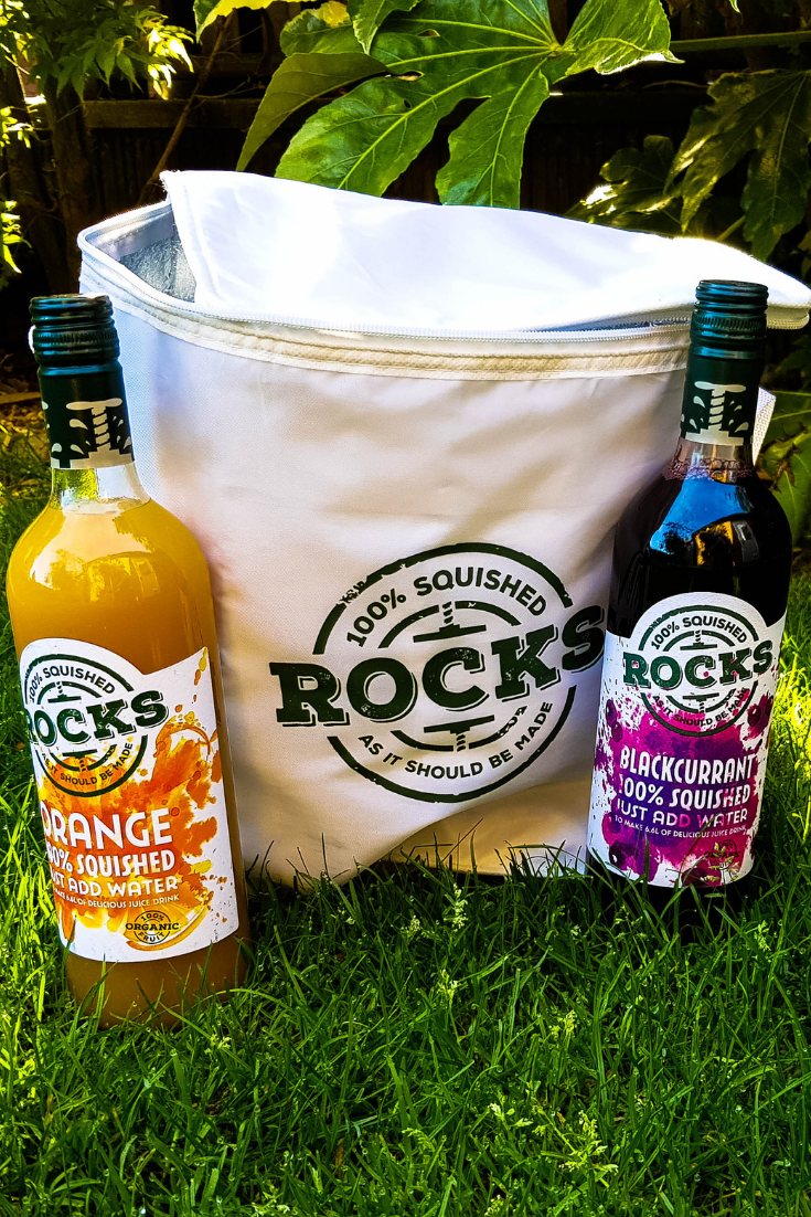 a white rocks drinks cool bag with a bottle of orange and bottle of blackcurrant drink either side