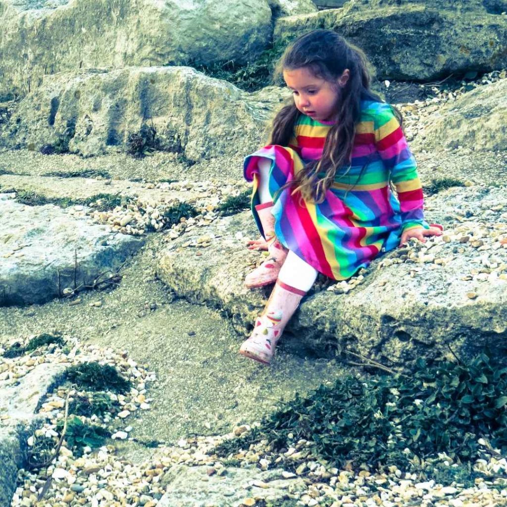 Alyssa sat on a rock wearing a Childrensalon rainbow dress